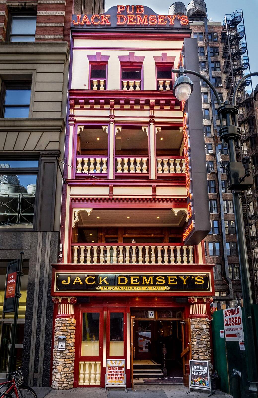 Facade of Jack Demsey's pub and restaurant with neon signs, stone pillars, and outdoor signs on a city street.